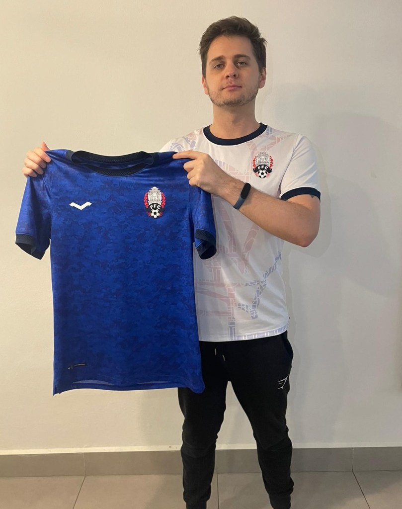 Frazer MacRobert, founder of Clan United, holding up the Cambodian National Football team Home top 22/23 - while wearing the away top for the same year—designed for Varaman and FFC.